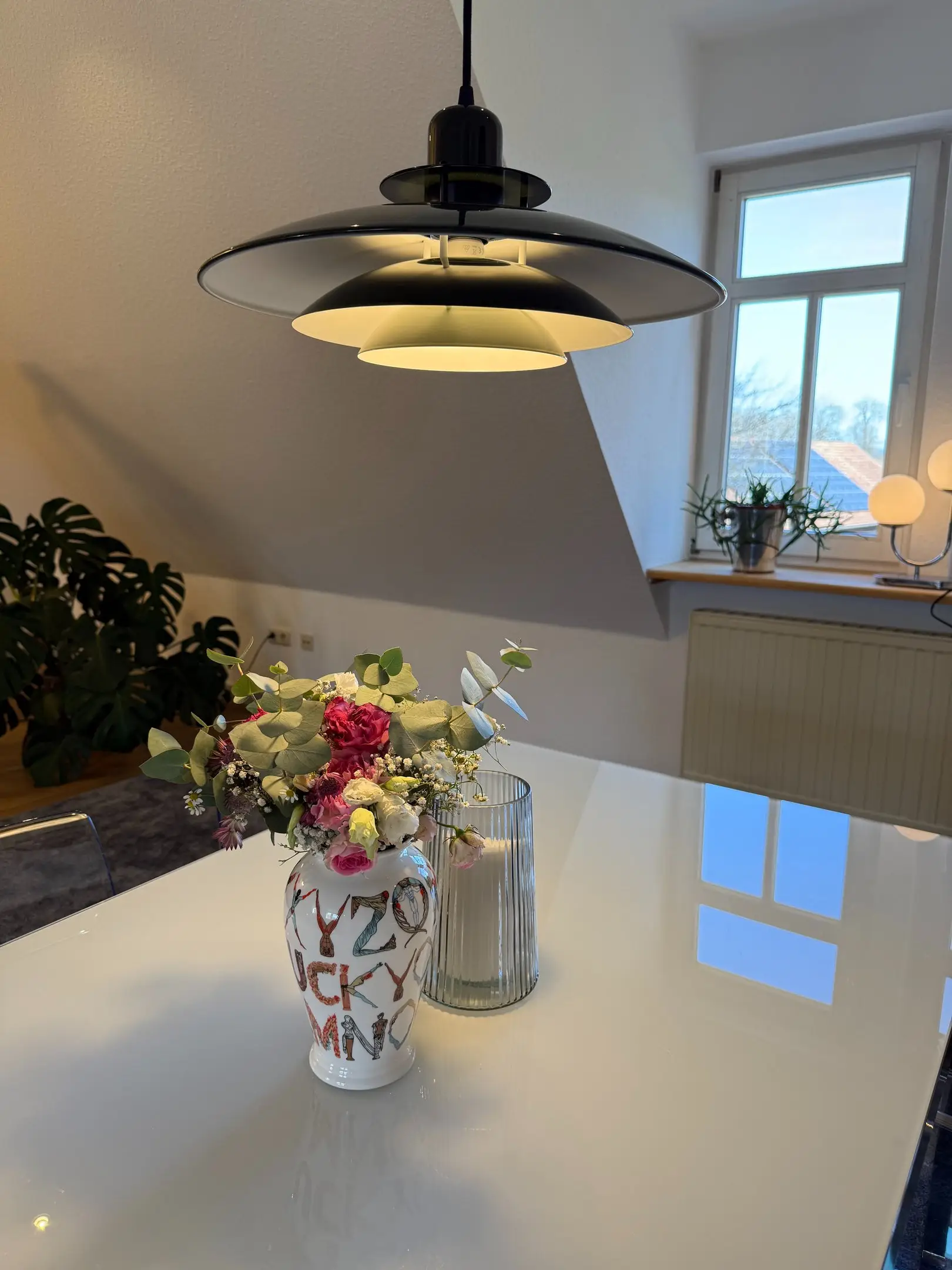Esstisch mit Blumenstrauß unter einer Designer-Hängeleuchte