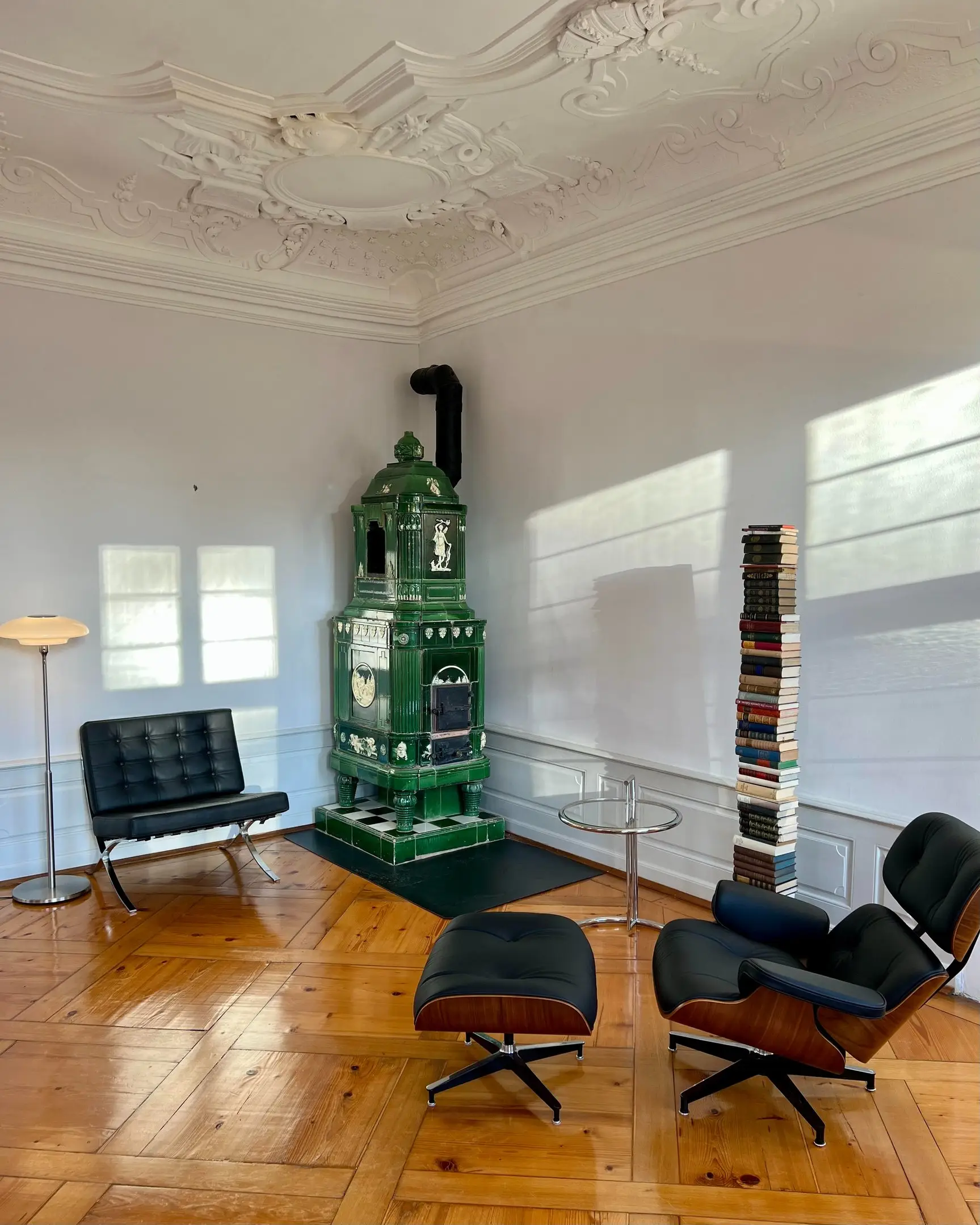 Grüner Kachelofen mit Designer-Loungesesseln auf Parkett