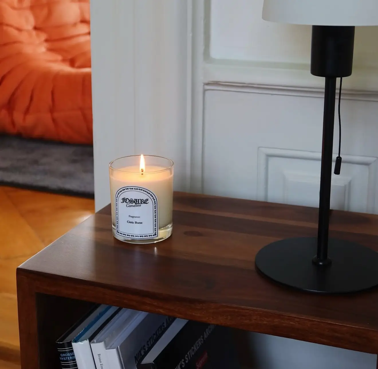 Brennende Kerze auf einem Holz-Sideboard neben einer schwarzen Tischlampe