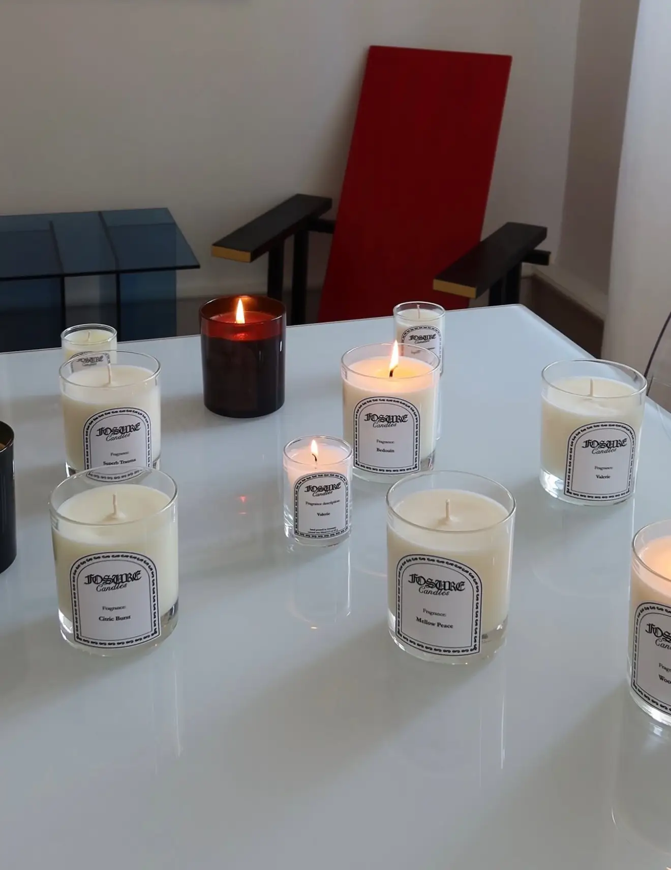 Brennende Kerzen auf einem weißen Tisch vor einem rot-blauen Designstuhl