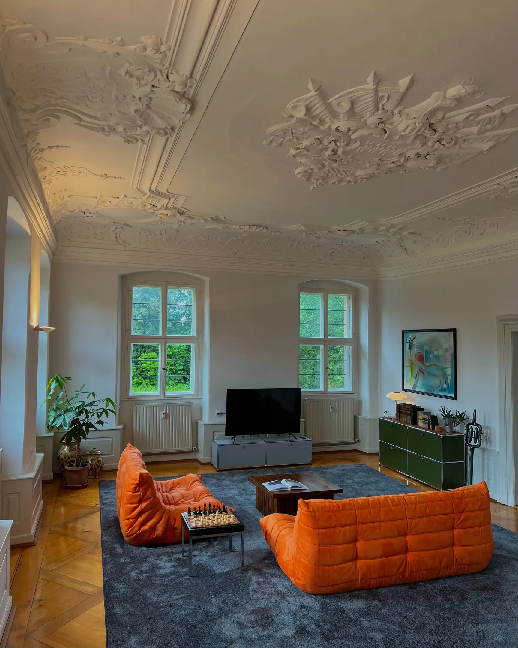 Salon mit barocker Stuckdecke, orangefarbenen Sofas und hohen Fenstern