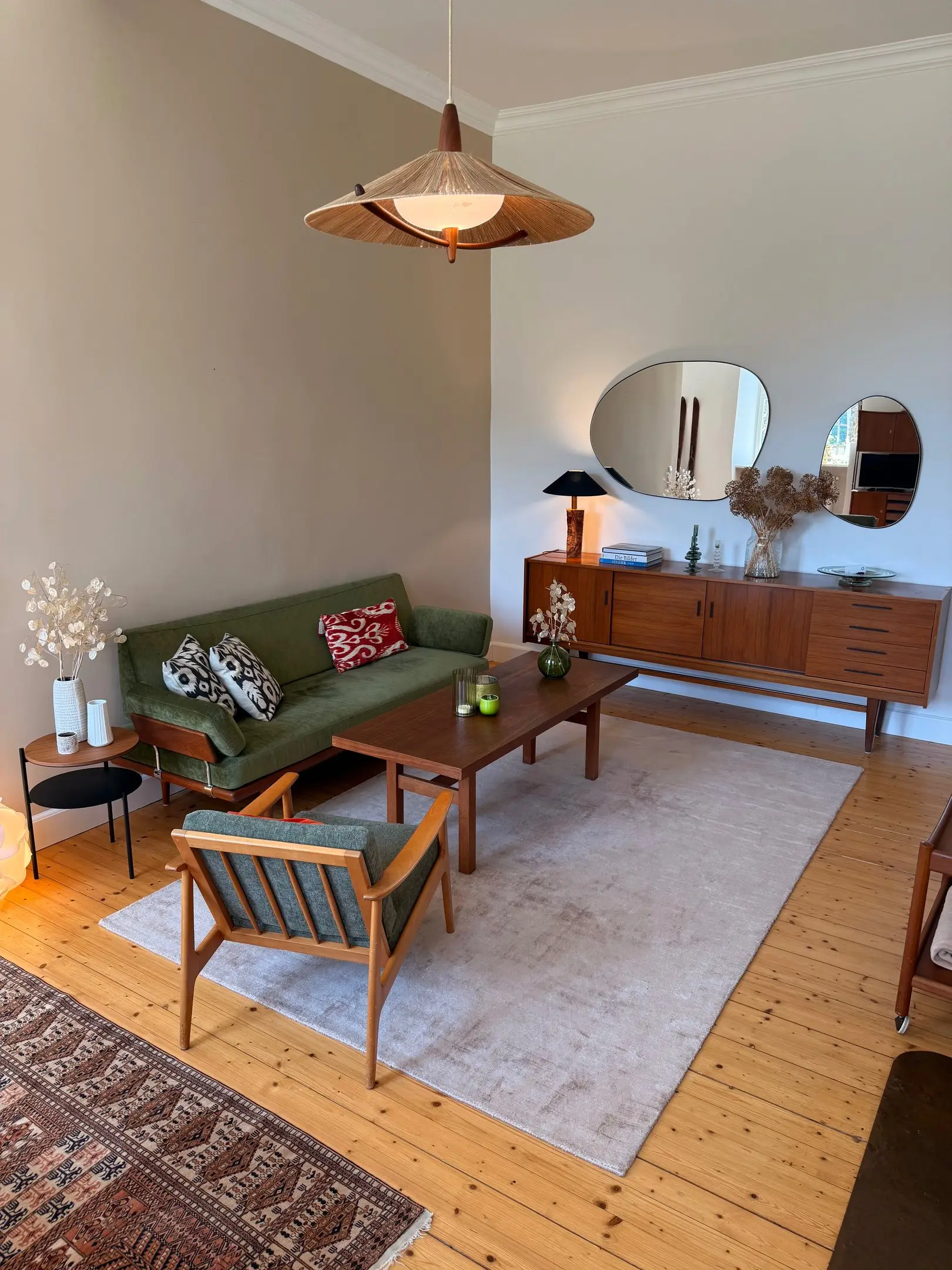 Wohnzimmer mit grünem Sofa, Teak-Sideboard und Orientteppich